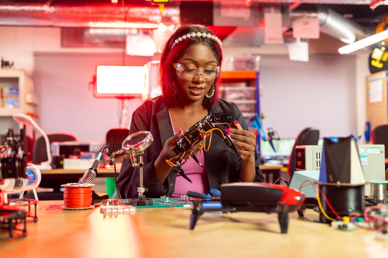 Initiatives Black female engineer at desk assembling drones, showcasing electronics and technology in a modern lab setting.