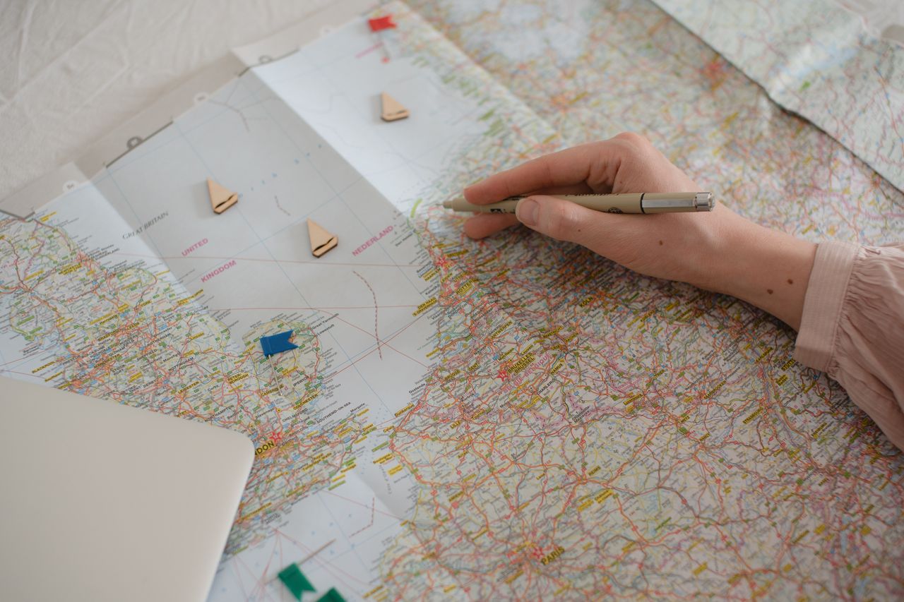 Hand holding pen over Europe map, planning travel route with markers.